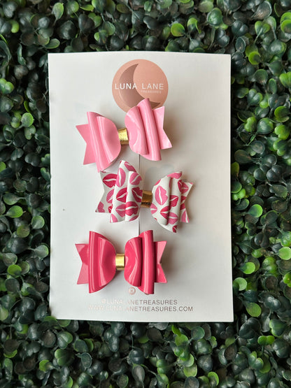  Enhance your daughter's fashion with our Pink Kisses Mini Bow Set! Each set contains 3 charming bows, each measuring 2.5 inches wide and precisely positioned on an alligator clip or nylon headband. Add a dose of adorability to any ensemble and let her exude self-assuredness. These bows add a touch of charm to any outfit, with each bow measuring 2.5 inches wide and securely attached to either an alligator clip or nylon headband. Guaranteed to make your daughter radiate confidence and style.