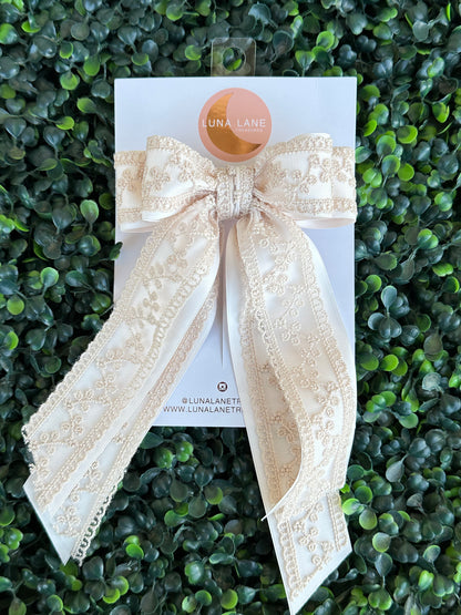 Enhance your hairstyle with the tan Coquette Hair Bow. This 5 inch wide and 8 inch long hair bow is made with delicate lace and satin matte ribbon for a sophisticated touch. Add a touch of elegance to any outfit with this stylish hair accessory.     comes attached to a French Barrett